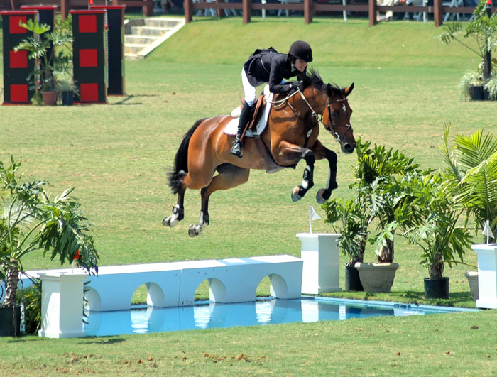 amazona saltando una ría con un caballo castaño en un concurso hípico