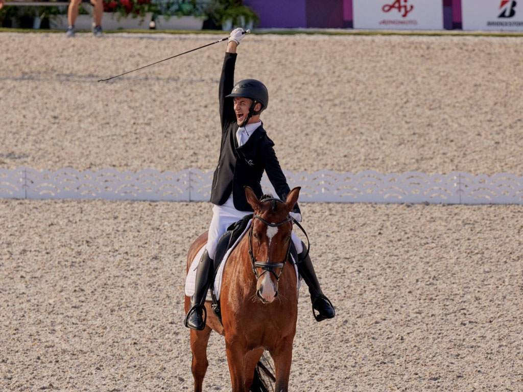 jinete paralímpico letón Rihards Skinus con el brazo en alto mientras monta a caballo saliendo de la pista tras una buena reprise